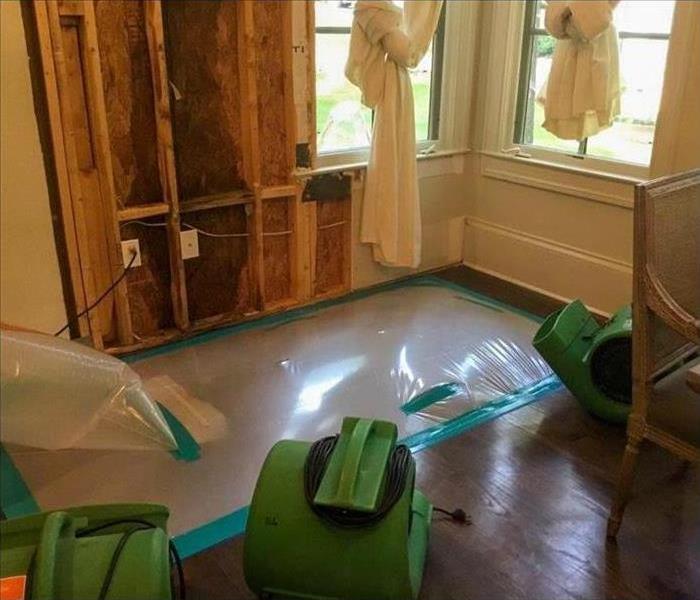 Air movers inside a home, plastic carpet placed on floor, drying equipment, drywall removal.